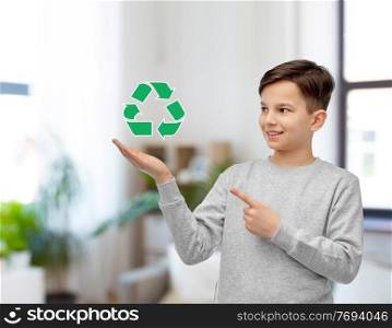 eco living, environment and sustainability concept - smiling boy showing green recycling sign over home room background. smiling boy showing green recycling sign