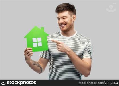 eco living, environment and sustainability concept - smiling young man in striped t-shirt holding green house icon over grey background. smiling young man holding green house icon