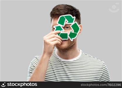 eco living, environment and sustainability concept - smiling young man in striped t-shirt holding green recycling sign over grey background. smiling young man holding green recycling sign