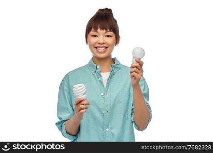 eco living, inspiration and sustainability concept - portrait of happy smiling young asian woman in turquoise shirt holding energy saving lighting bulb over grey background. asian woman holding energy saving lighting bulb