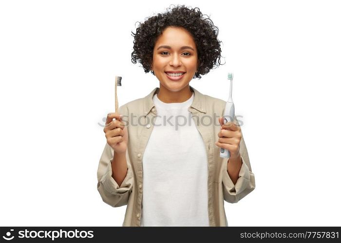 eco living, zero waste and sustainability concept - portrait of happy smiling young woman comparing wooden and electric toothbrushes over white background. woman comparing wooden and electric toothbrushes