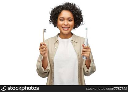 eco living, zero waste and sustainability concept - portrait of happy smiling young woman comparing wooden and electric toothbrushes over white background. woman comparing wooden and electric toothbrushes