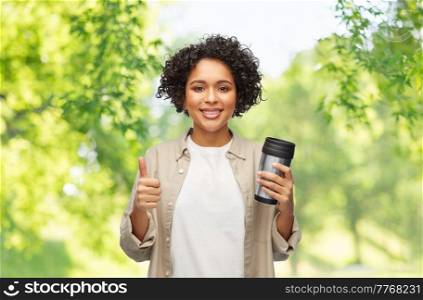 eco living, zero waste and sustainability concept - portrait of happy smiling woman with thermo cup or tumbler for hot drinks showing thumbs up gesture over green natural background. woman with thermo cup or tumbler for hot drinks