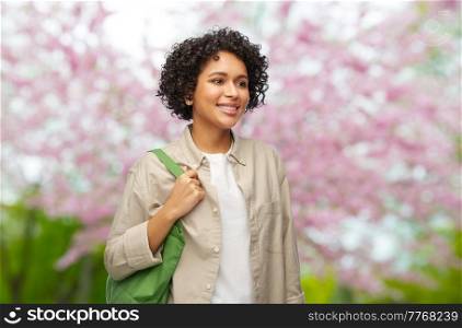 eco living, zero waste and sustainability concept - portrait of happy smiling woman with green reusable canvas bag for food shopping over blooming tree in spring garden background. woman with reusable canvas bag for food shopping