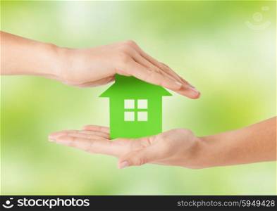 eco, people and real estate concept - close up of woman hands holding green house over natural background