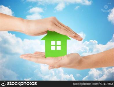eco, people and real estate concept - close up of woman hands holding green house over blue sky and clouds background