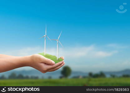 Eco power concept. Wind turbines and globe in human hand over blue sky background.