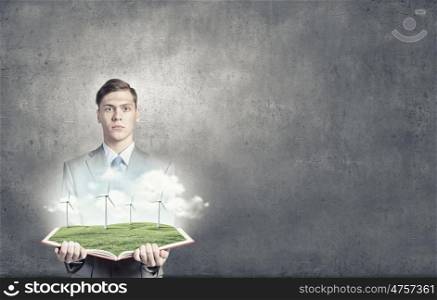 Ecological concept. Young man in suit holding opened book with windmills