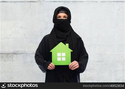 ecology and people concept - muslim woman in hijab with green house over gray concrete wall background. muslim woman in hijab with green house over white