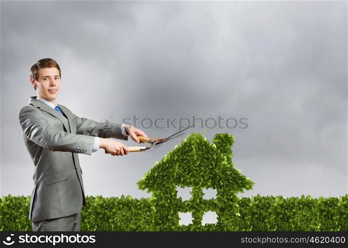 Ecology concept. Young businessman cutting green bush in shape of house