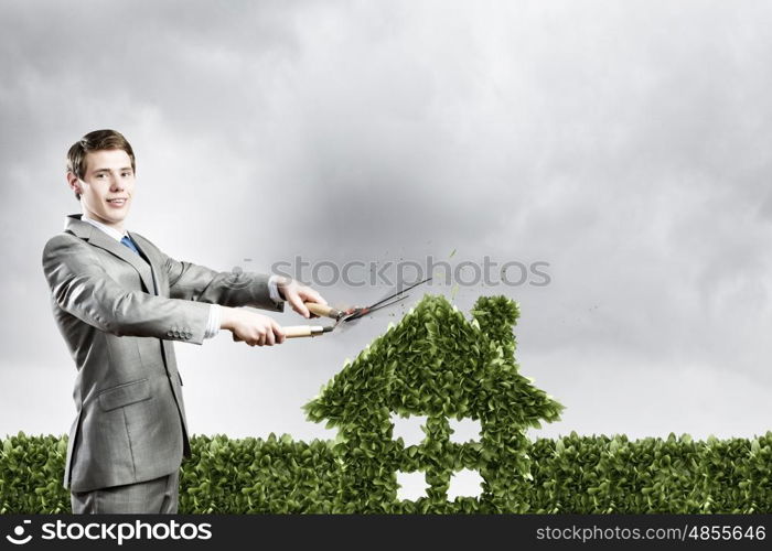 Ecology concept. Young businessman cutting green bush in shape of house