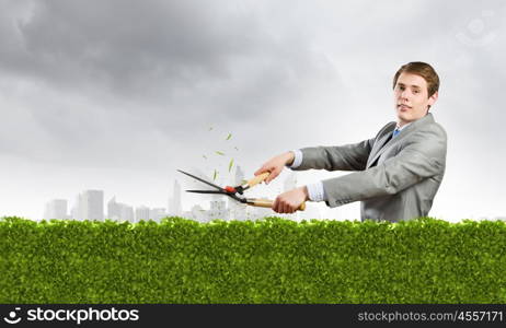 Ecology concept. Young businessman cutting green bush with grass cutter