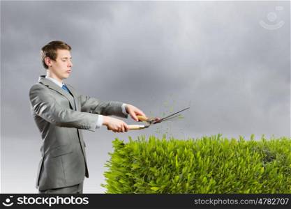 Ecology concept. Young businessman cutting green bush with grass cutter