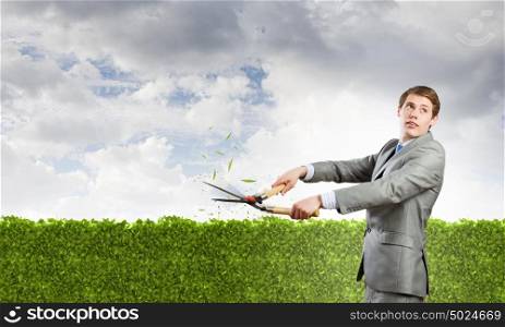 Ecology concept. Young businessman cutting green bush with grass cutter