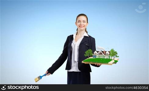Ecology concept. Young woman holding paint brush and wooden frame with house model