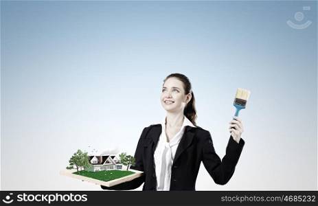 Ecology concept. Young woman holding paint brush and wooden frame with house model