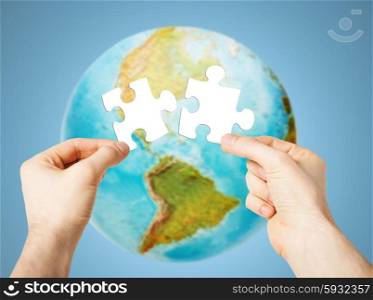 ecology, energy saving, people and environment concept - close up of male hands trying to connect white puzzle pieces over earth globe on blue background