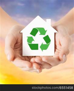 ecology, environment and conservation concept - close up of hands holding house with green recycling sign over evening sky background. hands holding house with green recycling sign. hands holding house with green recycling sign