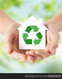 ecology, environment and conservation concept - close up of hands holding house with green recycling sign over natural background. hands holding house with green recycling sign. hands holding house with green recycling sign