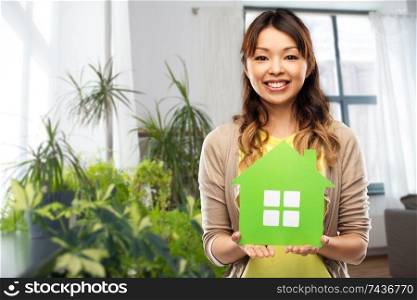 ecology, environment and mortgage concept - happy asian young woman with green house over home background. happy asian woman with green house at home