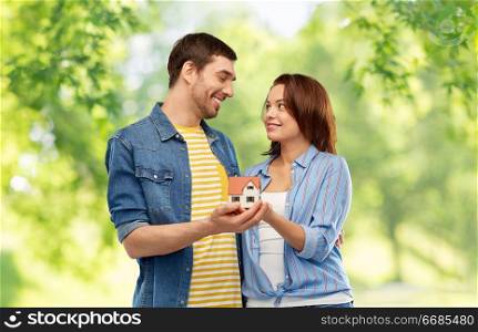 ecology, environment and mortgage concept - smiling couple holding house model over green natural background. smiling couple holding house model