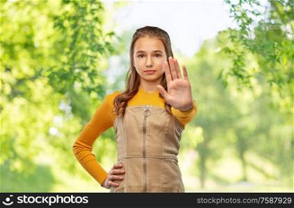ecology, prohibition and people concept - teenage girl making stopping gesture over green natural background. teenage girl making stopping gesture
