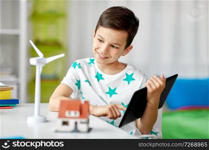 ecology, technology and energy saving concept - smiling boy with tablet pc computer, toy house model and wind turbine at home. boy with tablet, toy house and wind turbine