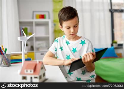 ecology, technology and energy saving concept - smiling boy with tablet pc computer, toy house model and wind turbine at home. boy with tablet, toy house and wind turbine