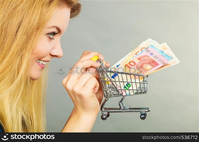 Economy, buying things, customer concept. Happy smiling woman holding shopping cart with euro money inside. Happy woman holding shopping cart with money