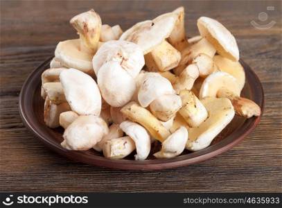 Edible wild mushrooms on a wooden background. Forest cleaned mushrooms in a clay plate.