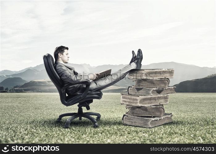 Education advantage. Young confident businessman sitting in chair with book in hands