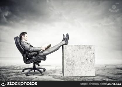 Education advantage. Young confident businessman sitting in chair with book in hands