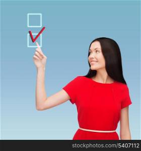 education and business concept - attractive young woman in red dress pointing her finger at red checkmark in checkbox