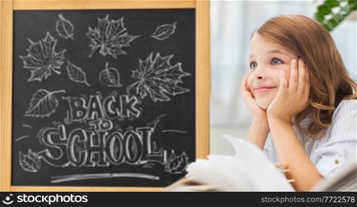 education and children concept - little student girl with books over chalk board with back to school lettering on background. student girl with books over school chalkboard