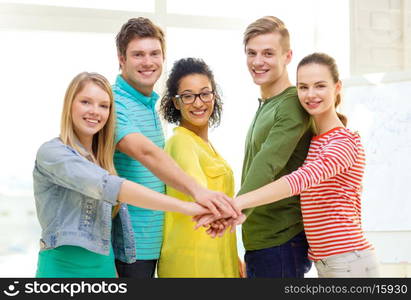 education and friendship concept - five smiling students with hands on top of each other