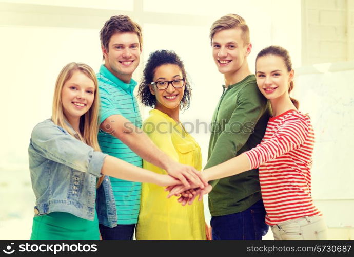 education and friendship concept - five smiling students with hands on top of each other