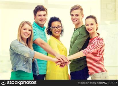 education and friendship concept - five smiling students with hands on top of each other