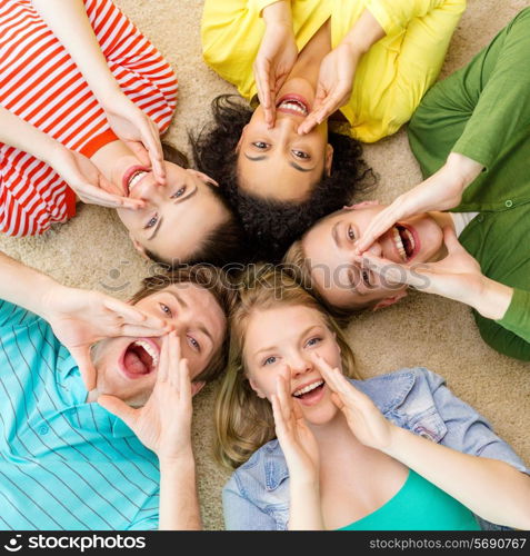 education and happiness concept - group of young smiling people lying down on floor in circle screaming and shouting