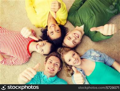 education and happiness concept - group of young smiling people lying down on floor in circle and showing thumbs up