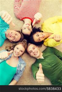 education and happiness concept - group of young smiling people lying down on floor in circle and showing thumbs up