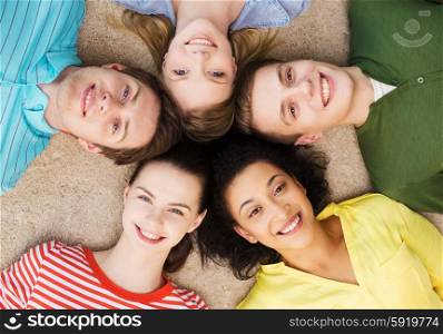 education and happiness concept - group of young smiling people lying down on floor in circle. group of smiling people lying down on floor