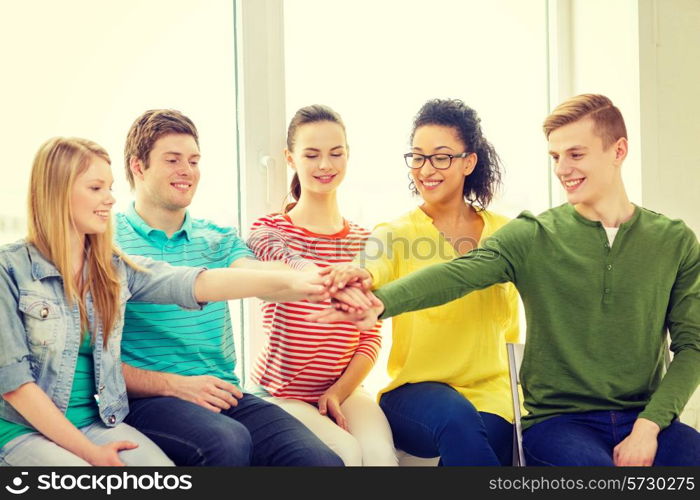 education and happiness concept - smiling students at school with hands on top of each