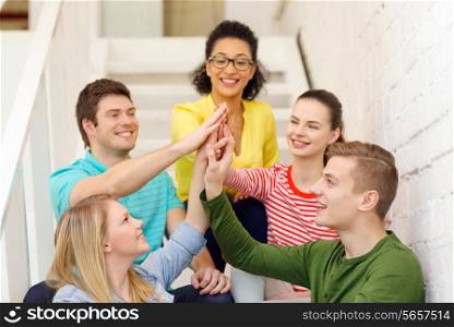 education and happiness concept - smiling students making high five gesture sitting on staircase