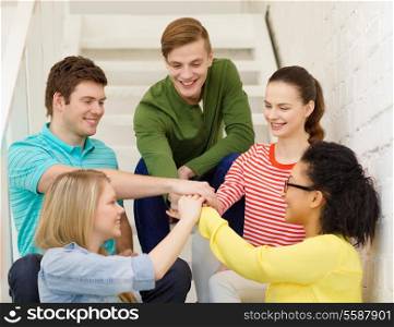 education and happiness concept - smiling students with hands on top of each other sitting on staircase