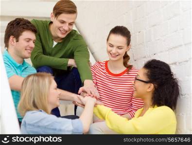 education and happiness concept - smiling students with hands on top of each other sitting on staircase