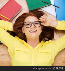education and home concept - smiling redhead female student in eyeglasses lying on floor