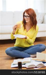 education and home concept - smiling student eating hamburger and doing homework at home