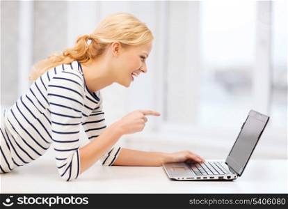 education and internet concept - smiling student girl pointing her finger at laptop screen in college