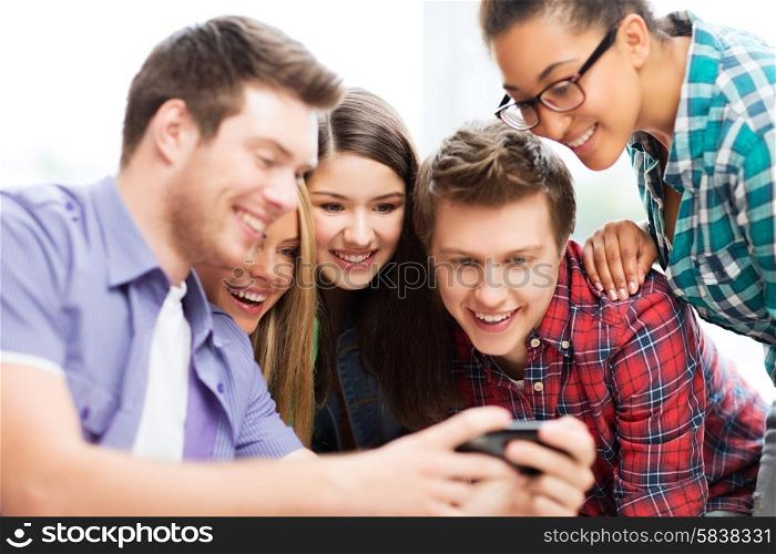 education and internet concept - smiling students looking at smartphone at school