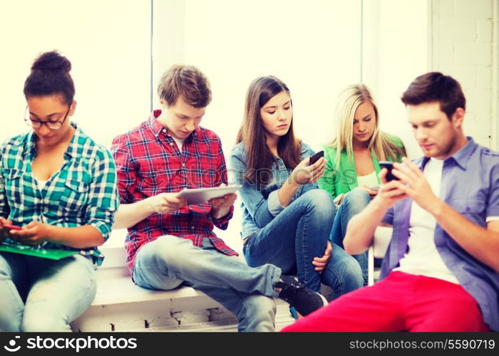 education and internet concept - students looking at their phones and tablet pc at school